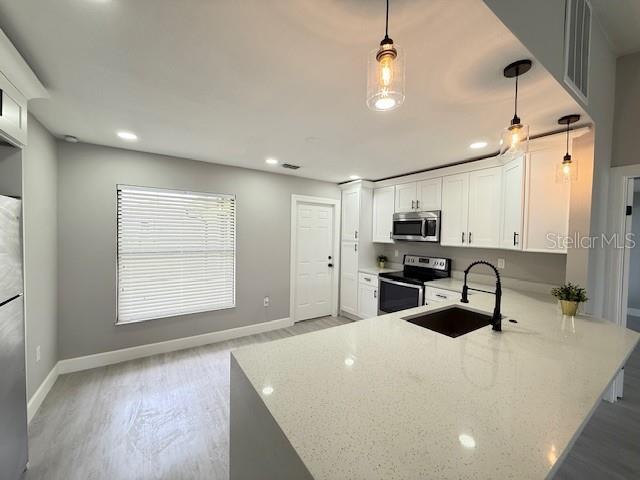 202 Cobalt Dr, Kissimmee, FL 34758 - kitchen with stainless steel appliances, light stone countertops, white cabinets, light wood-style flooring, and a peninsula