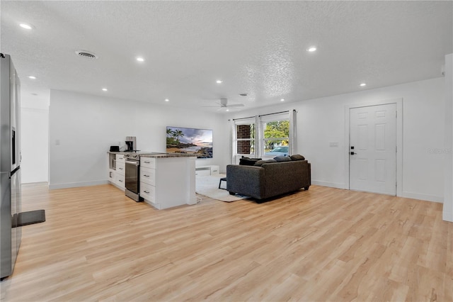 living room with a textured ceiling, ceiling fan, and light hardwood / wood-style flooring