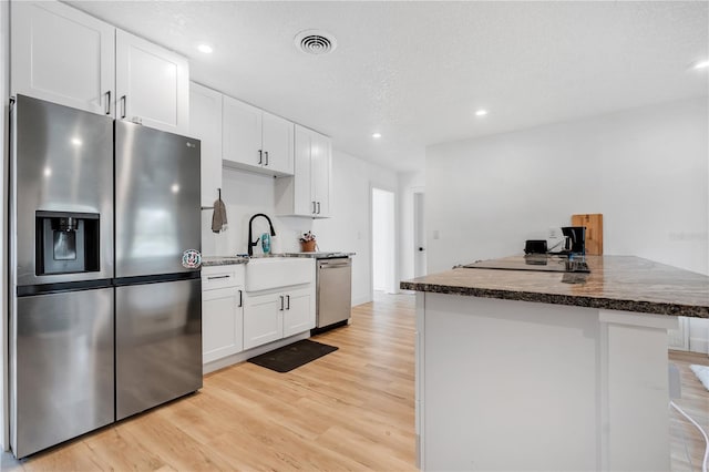 kitchen featuring stainless steel appliances, sink, white cabinets, a textured ceiling, and light hardwood / wood-style flooring