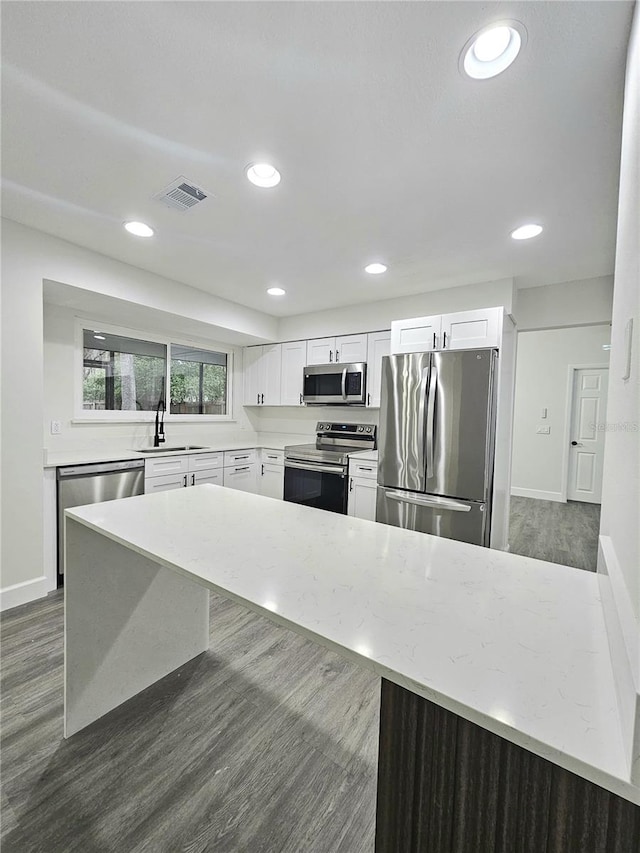 kitchen featuring stainless steel appliances, white cabinetry, light stone counters, and dark wood-type flooring