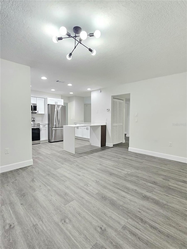 unfurnished living room with a textured ceiling, light hardwood / wood-style flooring, and an inviting chandelier