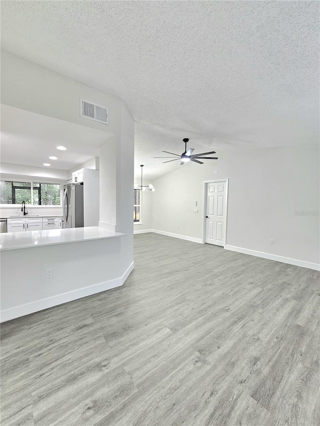 unfurnished living room featuring a textured ceiling, hardwood / wood-style floors, sink, and ceiling fan with notable chandelier