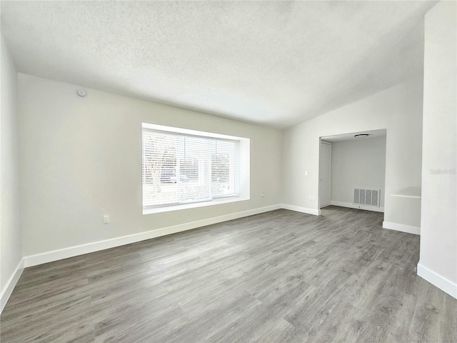 unfurnished room featuring lofted ceiling, light wood-type flooring, and a textured ceiling