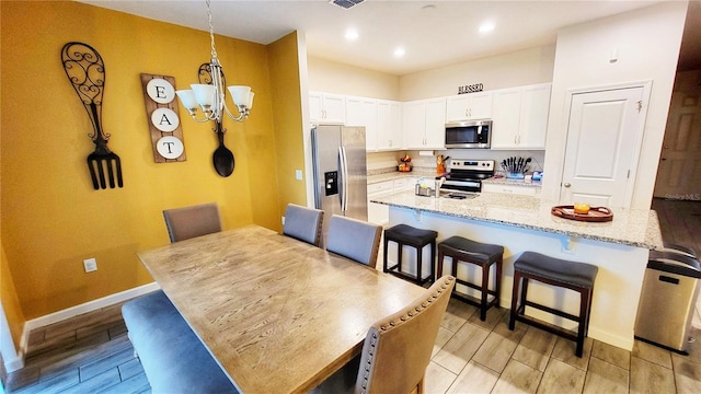 kitchen featuring stainless steel appliances, white cabinets, light stone counters, a breakfast bar area, and a kitchen island with sink