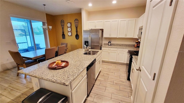 kitchen with stainless steel appliances, sink, white cabinets, light stone counters, and a kitchen island with sink