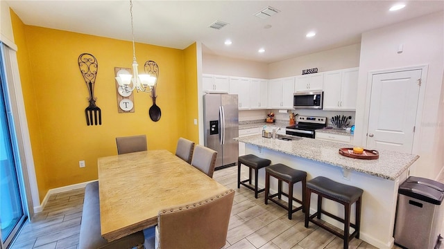 kitchen featuring light stone counters, an island with sink, a kitchen bar, white cabinetry, and appliances with stainless steel finishes