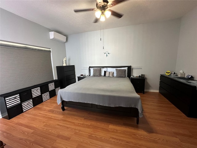 bedroom featuring a textured ceiling, a wall unit AC, ceiling fan, and hardwood / wood-style floors