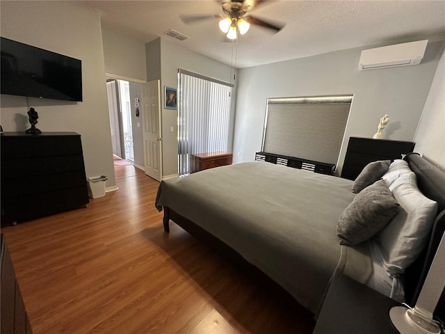 bedroom featuring hardwood / wood-style floors, an AC wall unit, and ceiling fan