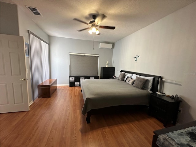 bedroom featuring an AC wall unit, ceiling fan, a textured ceiling, and hardwood / wood-style floors