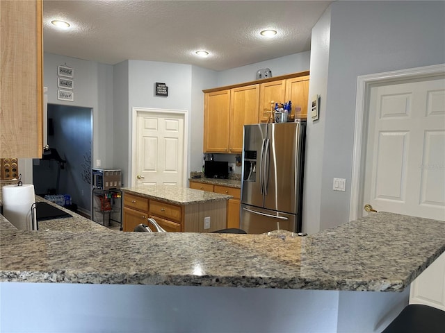 kitchen with light stone countertops, a textured ceiling, stainless steel fridge with ice dispenser, and kitchen peninsula