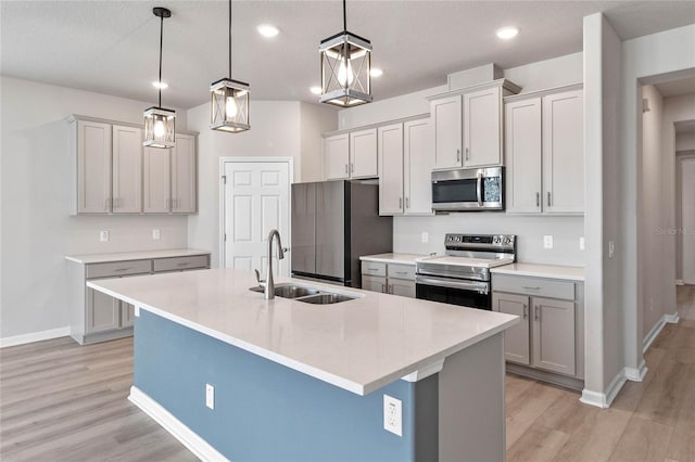 kitchen featuring hanging light fixtures, stainless steel appliances, a kitchen island with sink, gray cabinets, and sink