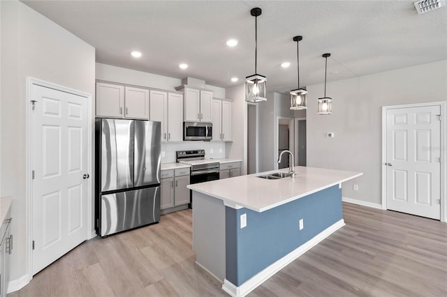 kitchen with hanging light fixtures, an island with sink, light wood-type flooring, appliances with stainless steel finishes, and sink