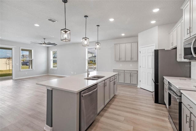 kitchen with stainless steel appliances, an island with sink, ceiling fan, pendant lighting, and sink