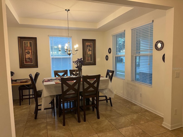 dining space featuring dark tile patterned flooring, a chandelier, and a tray ceiling