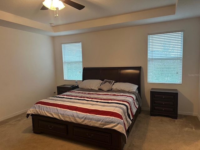 bedroom featuring ceiling fan, light colored carpet, and a tray ceiling