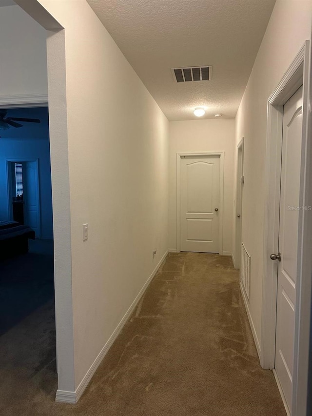 hallway with a textured ceiling and dark colored carpet