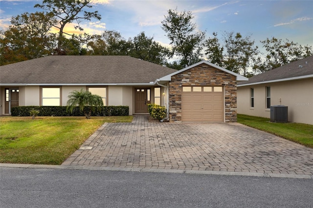 ranch-style house with a garage, central air condition unit, and a lawn