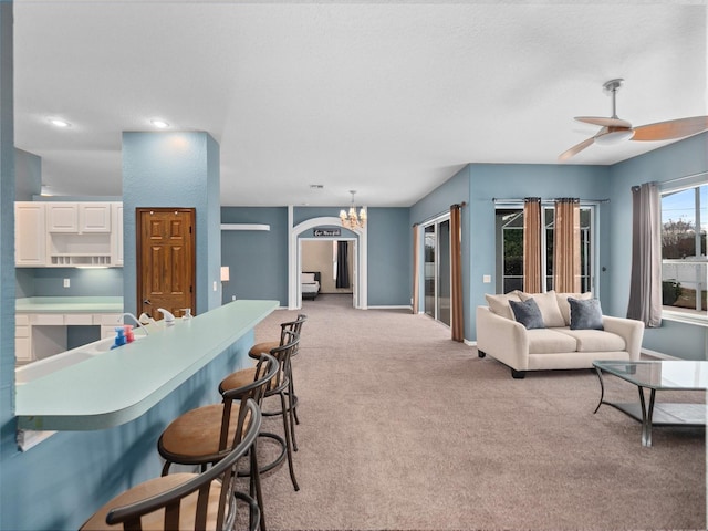 carpeted living room with ceiling fan with notable chandelier and sink