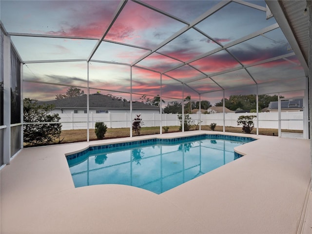 pool at dusk featuring glass enclosure and a patio