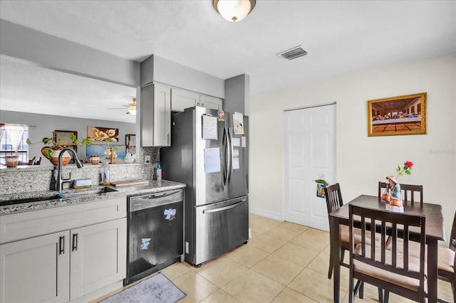 kitchen with light tile patterned flooring, dishwasher, sink, stainless steel fridge, and light stone countertops