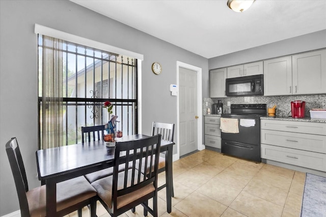 kitchen with gray cabinets, decorative backsplash, light tile patterned floors, black appliances, and light stone countertops