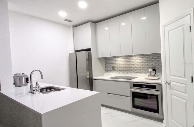 kitchen with white cabinets, stainless steel appliances, kitchen peninsula, sink, and tasteful backsplash