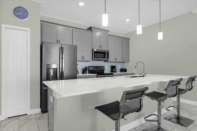 kitchen featuring appliances with stainless steel finishes, an island with sink, sink, backsplash, and a breakfast bar area