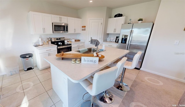 kitchen featuring appliances with stainless steel finishes, a breakfast bar, white cabinets, and a center island with sink