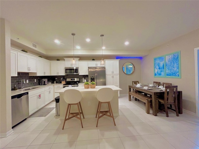 kitchen featuring white cabinets, a kitchen island, decorative light fixtures, stainless steel appliances, and sink