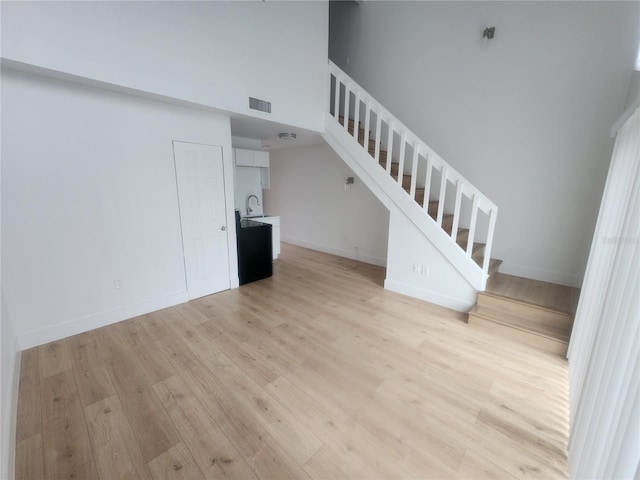 unfurnished living room with a high ceiling, sink, and light wood-type flooring