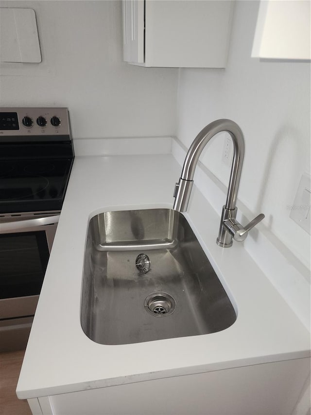 interior details featuring white cabinetry, stainless steel electric range oven, and sink