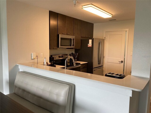 kitchen featuring stainless steel appliances, a textured ceiling, kitchen peninsula, and dark brown cabinetry