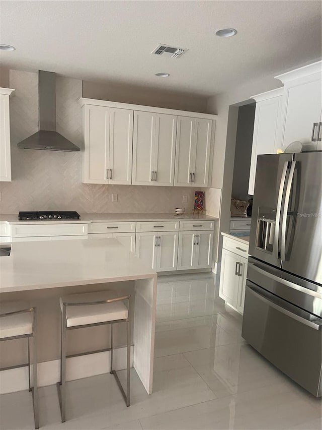 kitchen featuring tasteful backsplash, white cabinetry, stainless steel appliances, light tile patterned floors, and wall chimney exhaust hood