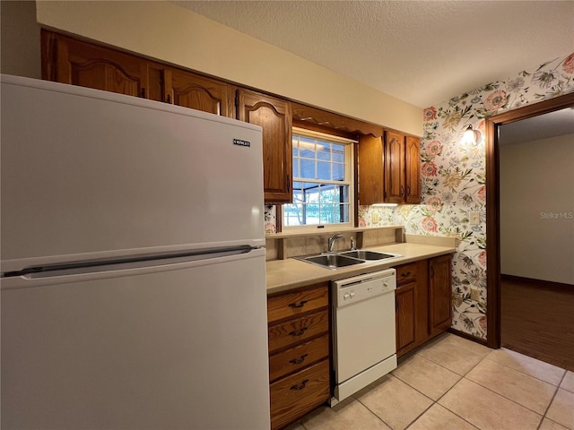 kitchen with sink, white appliances, a textured ceiling, and light tile patterned flooring