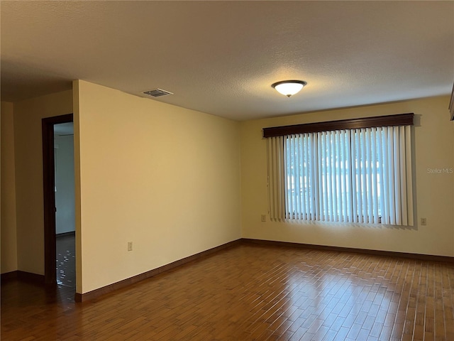 spare room featuring a textured ceiling and dark hardwood / wood-style floors