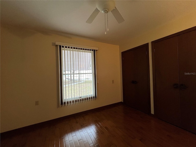 unfurnished bedroom with ceiling fan, multiple closets, and dark hardwood / wood-style flooring