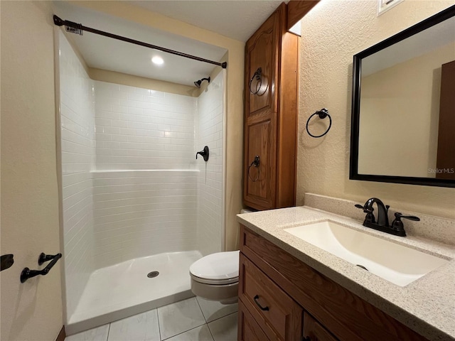 bathroom with tiled shower, vanity, toilet, and tile patterned flooring