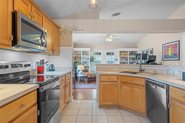 kitchen featuring sink, light tile patterned floors, appliances with stainless steel finishes, a textured ceiling, and vaulted ceiling