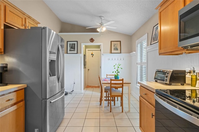 kitchen with vaulted ceiling, appliances with stainless steel finishes, light tile patterned floors, ceiling fan, and a textured ceiling