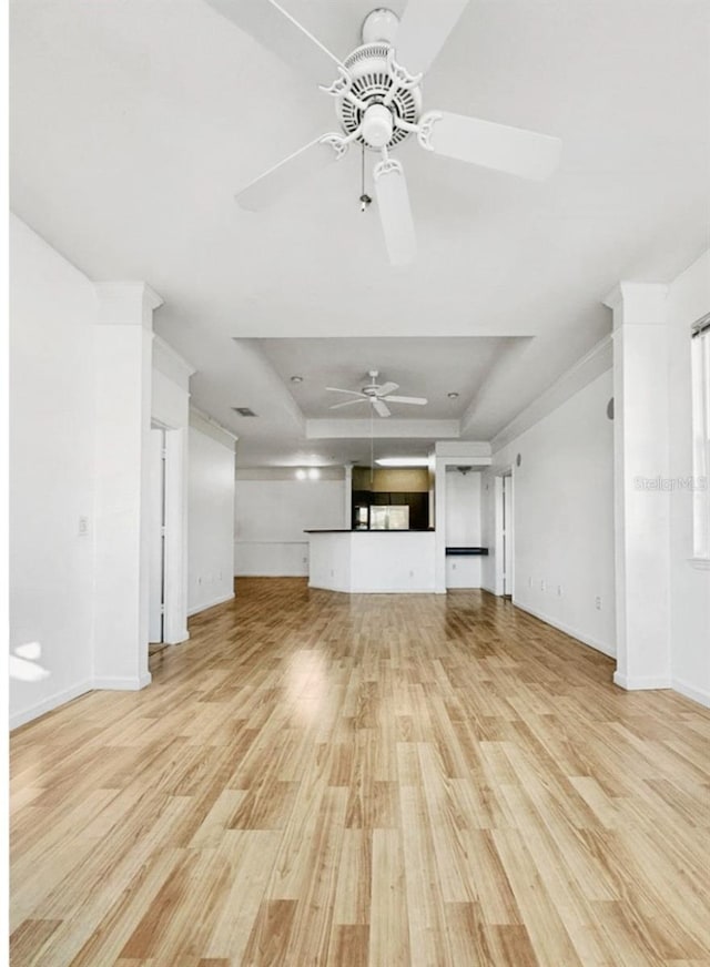 unfurnished living room featuring ceiling fan, a raised ceiling, and light wood-type flooring