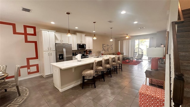 kitchen featuring a center island with sink, appliances with stainless steel finishes, hanging light fixtures, a kitchen bar, and white cabinets