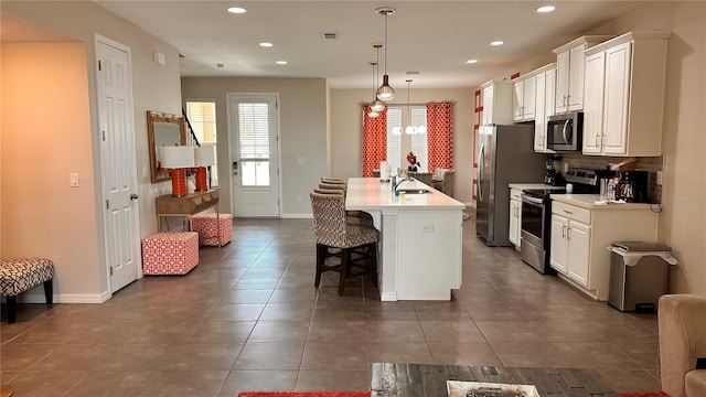 kitchen with decorative light fixtures, white cabinetry, a center island with sink, a breakfast bar, and appliances with stainless steel finishes