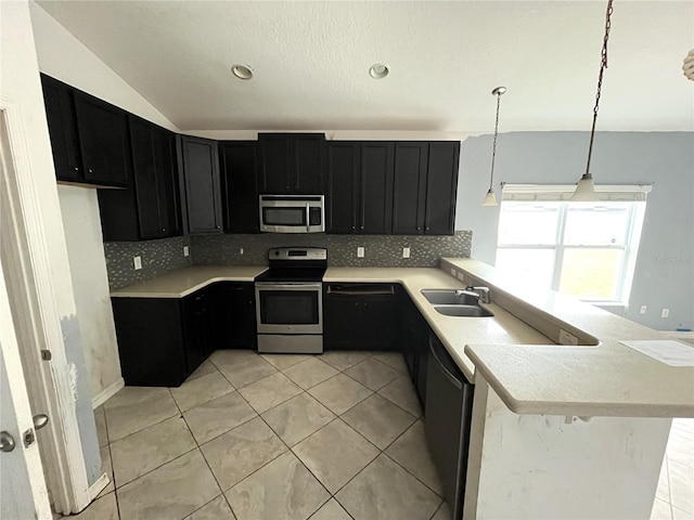 kitchen featuring kitchen peninsula, stainless steel appliances, decorative light fixtures, vaulted ceiling, and sink