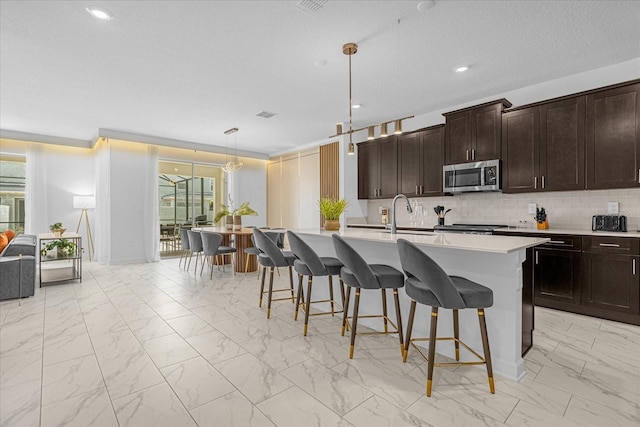 kitchen featuring tasteful backsplash, pendant lighting, a center island with sink, sink, and a kitchen breakfast bar