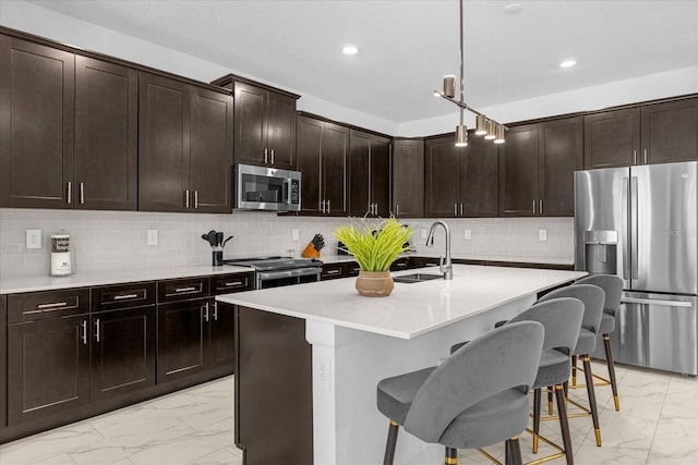 kitchen featuring appliances with stainless steel finishes, tasteful backsplash, sink, hanging light fixtures, and a kitchen island with sink