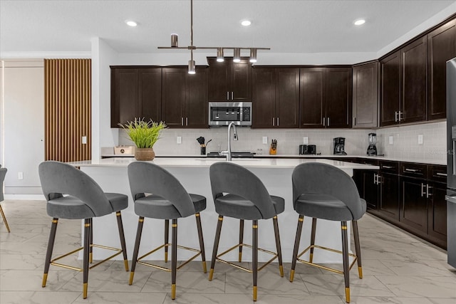 kitchen featuring a breakfast bar, dark brown cabinetry, tasteful backsplash, and an island with sink