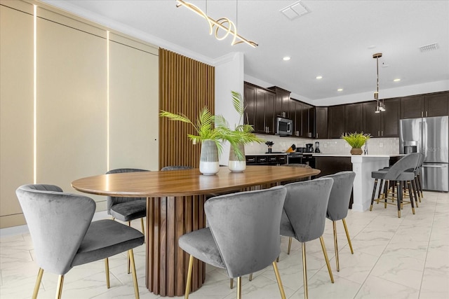 kitchen featuring decorative light fixtures, a breakfast bar, appliances with stainless steel finishes, and ornamental molding