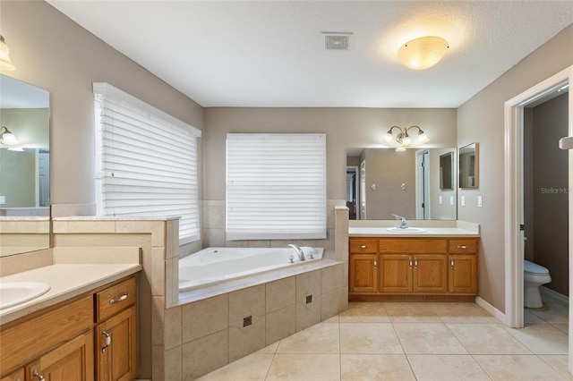 bathroom with toilet, vanity, tile patterned flooring, a textured ceiling, and a relaxing tiled tub