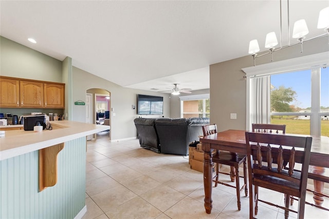 tiled dining space featuring a healthy amount of sunlight, vaulted ceiling, and ceiling fan with notable chandelier