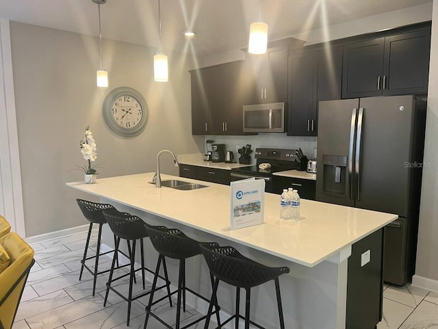 kitchen with decorative light fixtures, a center island with sink, sink, appliances with stainless steel finishes, and a kitchen breakfast bar